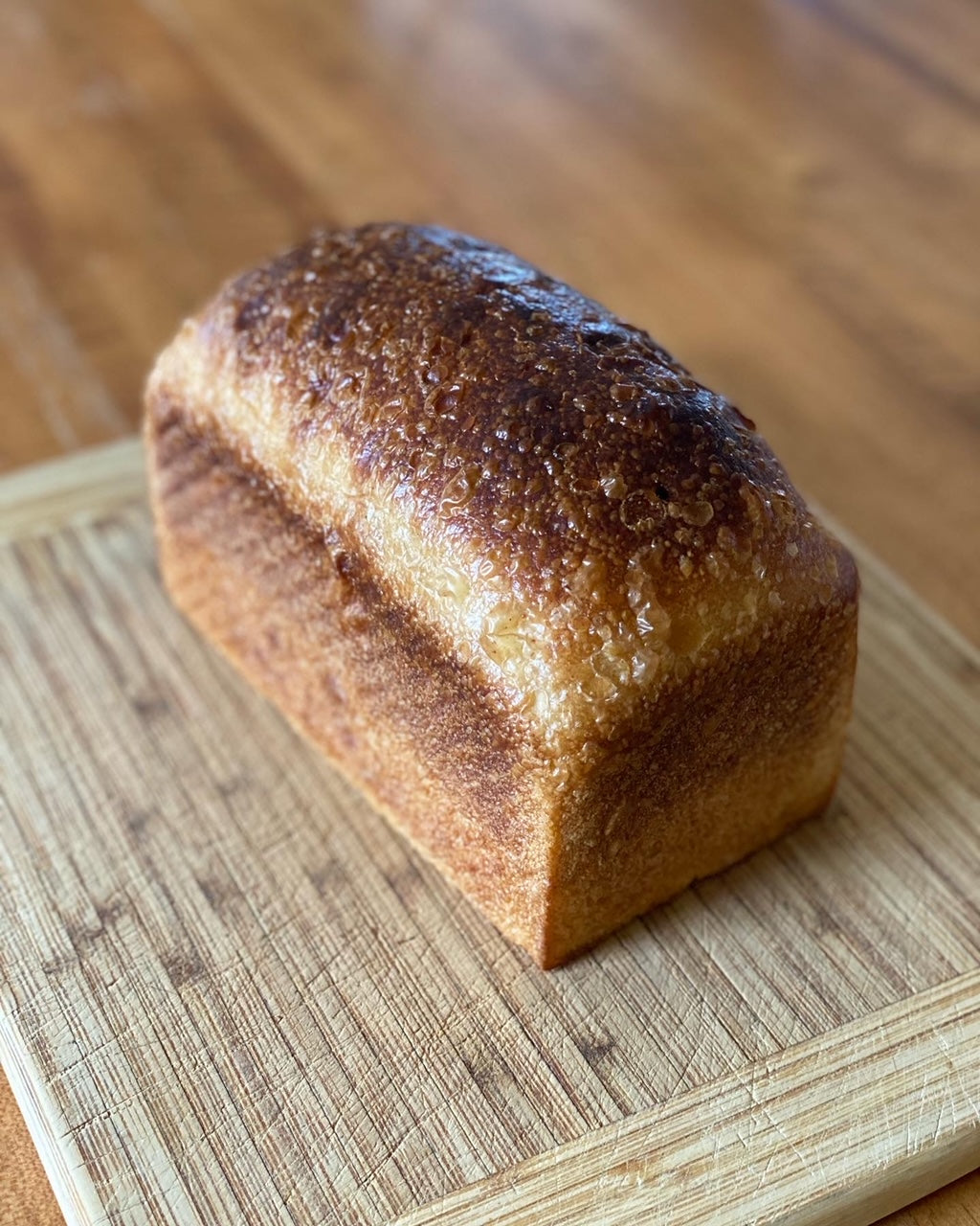 A loaf of golden-brown sourdough bread with a decorative score on the top crust.